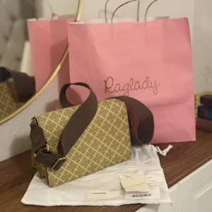 By Malene Birger beige axelväska - Snygg beige axelväska från By Malene Birger med klassiskt rutigt mönster och bred, brun axelrem. Väskan har två fack och guldfärgade metalldetaljer. Perfekt för dig som vill ha en stilren och trendig accessoar. Ny pris 3000kr!