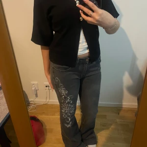 Gråa jeans med strass - Säljer ett par gråa jeans med snygga strassdetaljer i form av fjärilar på ena benet och blommor på andra. Jag är 164cm lång och de är lite långa på mig. Har lagt in en bild på fickorna också. 