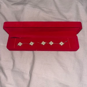 Guldigt armband med blommor - Superfint armband med fem blommiga berlocker i guldton, varje blomma har en pärlliknande detalj i mitten. Kedjan är tunn och elegant, perfekt för att ge en lyxig touch till din stil. Kommer i en snygg röd ask. Äkta silver , den har gått av men det går och laga.