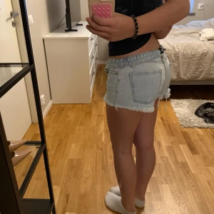 Ljusblåa jeansshorts med fransig kant - Säljer ett par ljusblåa jeansshorts med låg midja och rå, fransig kant nertill. Shortsen har klassiska fickor både fram och bak samt bälteshällor. Perfekta för sommaren och ger en avslappnad vibe. Har öppnat sig vid hörnet men går fortfarande att använda