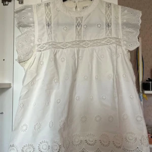 Vit broderad kortklänning från Pimkie - Superfin vit kortklänning från Pimkie med broderade blommor och spetsdetaljer. Klänningen har volangärmar, rund hals och knäppning bak. Perfekt för sommarens alla tillfällen och ger en romantisk vibe med sina söta detaljer.