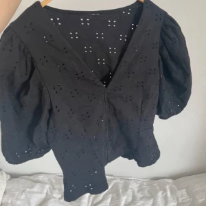 Svart blus med puffärm och broderi - Svart blus med v-ringning och korta puffärmar. Blusen har broderade hålmönster över hela tyget som ger en luftig känsla. Bra skick!!💞💞🤩🤩