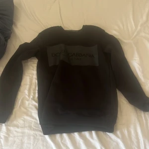 Svart Dolce & Gabbana sweatshirt XS - Svart sweatshirt från Dolce & Gabbana i storlek XS. Tröjan har en klassisk rund halsringning, långa ärmar och en stor svart logga framtill. Perfekt för dig som gillar stilrena och exklusiva plagg med streetkänsla.