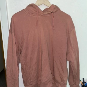 Rosa hoodie med huva och snörning - En enkel och snygg rosa hoodie med huva och snörning. Tröjan har lång ärm och ribbade muddar vid ärmslut och nederkant. Perfekt för chill dagar eller när du vill ha en avslappnad stil.