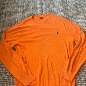 Orange tröja från Ralph Lauren - Snygg orange långärmad tröja från Ralph Lauren med blå broderad logga på bröstet. Slim fit-modell i mjuk pima bomull, perfekt för dig som gillar klassisk stil med en färgklick. Rund halsringning och ribbade muddar. Skriv ifall frågor uppkommer eller ifall du vill se fler bilder, kolla även gärna in min profil ❣️❣️