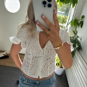 Vit broderad blus från Zara Woman - Superfin vit blus från Zara Woman med broderade detaljer och hålmönster. Blusen har korta volangärmar, v-ringning och knappar framtill. Perfekt till jeans för en fräsch och somrig look.