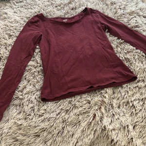 Vinröd långärmad topp från 157 - En enkel och stilren vinröd långärmad topp från 157. Modellen har rund halsringning och är tillverkad i mjuk bomull med lite stretch för en bekväm passform. Perfekt att matcha med jeans eller kjol för en clean look.