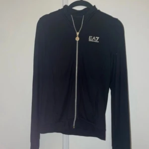 Svart EA7 kofta - Tunn kofta från Emporio Armani med märken på sidan av hela armen på båda sidorna. Använd en del men fortfarande bra skick och inga defekter.