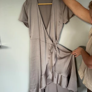 Beige omlottklänning från Neo Noir - Säljer en snygg beige omlottklänning från Neo Noir med korta ärmar och v-ringad hals. Klänningen har volangdetaljer längs nederkanten och knyt i midjan. Det är storlek M/L men passade även mig som är en S med hjälp av knutbanden❣️