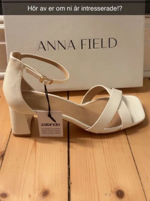 Vita klackskor från Anna Field - Snygga vita klackskor från Anna Field med bred klack, öppen tå och remmar över foten. Skorna har en justerbar ankelrem med spänne och en stilren design som passar perfekt till sommarens outfits.