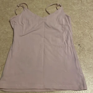 Ljusrosa linnetopp med smala band - Säljer en enkel och stilren ljusrosa linnetopp med tunna axelband och v-ringad hals. Toppen har en mjuk och slät yta, perfekt för varma dagar. Passar till både jeans och kjol för en avslappnad look.