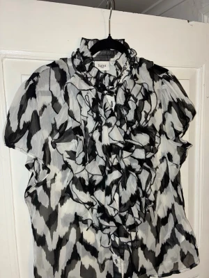 Vit och svart blus Saint Tropez - En vit och svart blus från Saint Tropez. Den är kortärmad och har volang längs knapparna framtill.