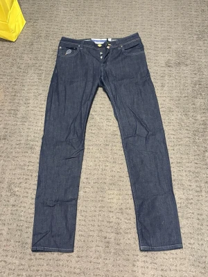 Jacob Cohën Nick Slim jeans blå - Säljer ett par mörkblå jeans från Jacob Cohën, modell Nick Slim. Jeansen har raka ben, klassisk femficksdesign och kontrastsömmar. Märkespatch i orange bak och detaljer i gult. Tillverkade i mjukt jeansmaterial med knappgylf.storlek 3-