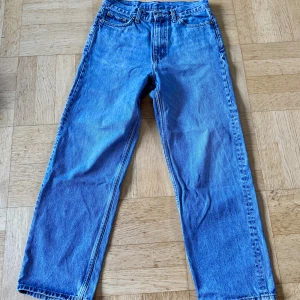 Blå Weekday Galaxy Loose Straight Jeans - Säljer ett par blå Galaxy Loose Straight Jeans från Weekday i storlek 27/30. Modellen har rak passform med loose stil och klassisk femficksdesign. Jeansen är tillverkade i bomull och har en snygg ljusblå tvätt. Perfekta för dig som gillar avslappnad look.