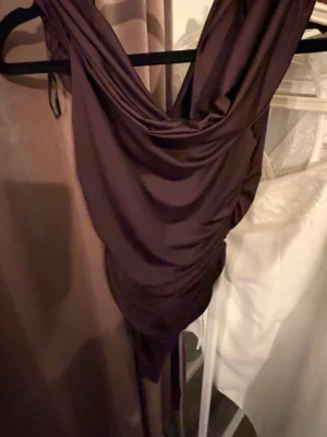 Vinröd body  - Säljer en vinröd body med snygg drapering och v-ringad hals. Bodyn har en elegant, glansig satinfinish och är figurnära med asymmetrisk nederdel. Perfekt för dig som gillar stilrena och trendiga plagg.