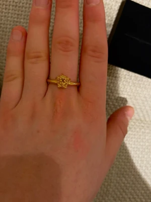 Guldfärgad Versace ring Medusa - Säljer en ikonisk guldfärgad ring från Versace med Medusa-huvud framtill. Ringen är i metall och har en clean, tunn ringband som gör den enkel att matcha med andra smycken. Kommer i original ask och äkthetsbevis. Aldrig använd, köpt för 1700 på outlet. 