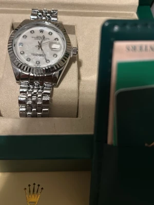 Oyster Perpetual Datejust klocka - Exklusiv automatisk klocka i rostfritt stål med räfflad bezel och jubileelänk. Silverfärgad urtavla med diamantmarkeringar samt datumfunktion.  Klockan säljs som fullset och levereras med originalbox, certifikat, kvitto samt påse. 41mm Mycket gott skick och väl omhändertagen. En tidlös och elegant klocka som passar både till vardag och fest. Helt ny. Priset kan diskuteras 🫡👍 