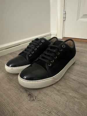 Svarta sneakers från Lanvin med lack - Lanvin sneakers i svart mocka med snygg lackad tå och vit platt sula. Skorna har snörning med svarta skosnören. Insidan är beige och sulan är märkt med Lanvin. Box ingår inte och finns inte kvitto. Skorna är i princip helt nya använt två gånger varför jag säljer skorna är för jag behöver pengar. Priset är ej hugget i sten