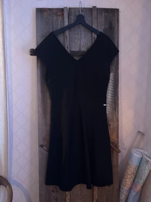 Svart kortklänning från Armani Exchange - Snygg svart klänning från Armani Exchange i storlek L. Klänningen har v-ringning både fram och bak, är ärmlös och har en klassisk, figurnära passform med lätt utställd kjol. Perfekt för dig som gillar stilrena och tidlösa plagg.