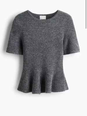 Grå stickad topp med volang - Säljer en grå stickad topp med korta ärmar och rund hals. Toppen har en snygg volangkant nedtill. Har bara använt en gång så den är nästan helt oanvänd 💞💞