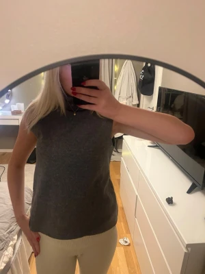 Mörkgrå polotopp ärmlös - Säljer en stilren mörkgrå polotopp med ärmlös design. Toppen har en hög krage och är gjord i ett mjukt material som känns skönt mot huden. Perfekt att matcha med jeans eller kjol för en clean look.