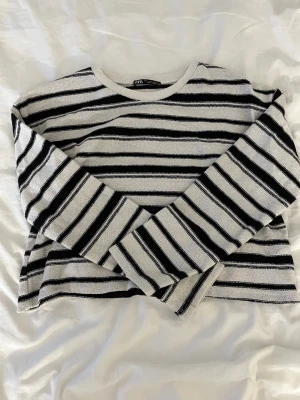 Randig croppad tröja från Zara - Säljer en croppad långärmad tröja från Zara med svart och vit randigt mönster. Tröjan har rund hals och är stickad. Perfekt för dig som gillar en chill och stilren look.