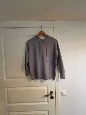 Bekväm grå huvtröja  -  Gråmelerad huvtröja i mjukt material. Den har en avslappnad passform, långa ärmar och en justerbar huva med dragsko. Perfekt för en avslappnad och bekväm stil.