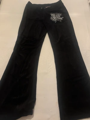 Svarta bootcut byxor Juicy Couture - Svarta bootcut byxor från Juicy Couture i mjuk velour med broderad logga framtill. Byxorna har snörning i midjan och fickor bak med metallöglor. Tyvärr blev bilderna lite dåliga med tanke på ljuset. Storleken på byxorna är S och dom är ämvända ungefär två gånger. 💗💗