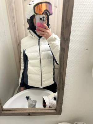 Vit och svart skidjacka - Säljer en fräsch skidjacka i vit och mörkgrå/svart färg med hel dragkedja framtill. Jackan har hög krage och är långärmad, perfekt för kalla dagar i backen. Skriv privat för mer bilder samt frågor❤️