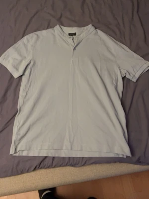 Ljusgrå t-shirt från Lefties Man - Säljer en ljusgrå t-shirt från Lefties Man i storlek S. T-shirten har korta ärmar, en liten ståkrage och två knappar vid halsen. Materialet är bomull och ger en skön och avslappnad känsla. Perfekt för dig som gillar enkel och clean stil.