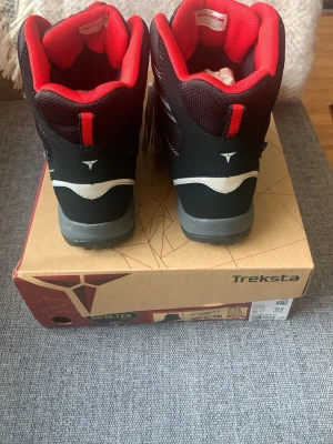 Svarta Treksta kängor strl 38 - Säljer ett par svarta och röda Treksta JR Cobra II GTX kängor i storlek 38. Skorna har grå sula, kardborreband och är tillverkade i slitstarkt syntetmaterial med Gore-Tex för vattentäthet. Perfekt för dig som vill ha bekväma och tåliga kängor med cool design. Nypris är även 999kr, så väldigt bra pris