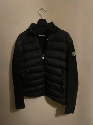 Moncler cardigan - En överfet cardigan med röda detaljer på sidan av jackan. Storlek L men passar bra på mig som brukar ha M. Håller värmen bra för dom som tål vintern annars en perfekt vår och höst jacka. Den tar bara plats i garderoben så pris går att diskutera vid snabb affär.Ärmarna har blivit lite noppriga med tiden och har inte ork att fixa det. Köpt i godtro men det visade sig att den var rëplic@. Men förutom det så är det en väldigt fin jacka!