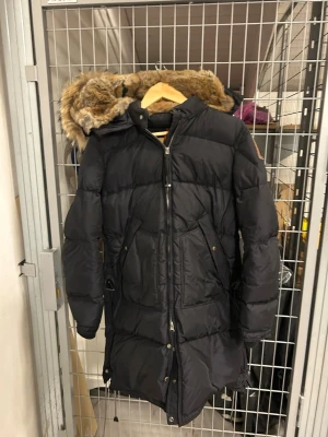Svart Parajumpers long bear  - Svart lång dunjacka från Parajumpers strl M,med fluffig päls på huvan och gul detalj vid kragen. Jackan har patch på ärmen. Kan gå ner i pris vid snabb affär