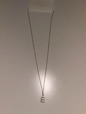 Edblad halsband - Bilderna visar ett halsband med ett E-format hänge i silverfärg och små glittriga stenar. I princip aldrig använt. Nypris 399kr.🥰