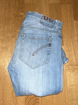 Replay ljusblå jeans med slitningar - Säljer ett par ljusblå Replay jeans med snygga slitningar och detaljer på både fram- och baksida. Jeansen har klassisk femficksdesign, knappgylf och coola sömmar på bakfickorna. Perfekt för dig som gillar en avslappnad och trendig look.