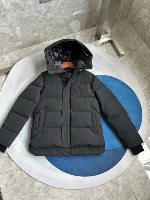 Canada Goose Macmillan Svart   - ALLA STORLEKAR OCH FÄRGER! Säljer en svart pufferjacka från Canada Goose med avtagbar huva och klassisk patch på ärmen. Jackan har dragkedja framtill, två stora fickor och ribbade muddar vid ärmsluten. Perfekt för kalla dagar och riktigt snygg till streetwear. KOMMER MED VÄSKA 