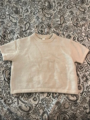 Beige stickad kortärmad tröja – mjuk & tidlös - Mjuk och skön stickad tröja i vit/krämfärgad nyans. Kortärmad modell med rund ribbad halsringning och rak passform som gör den lätt att matcha till både jeans, kjol eller kostymbyxor. Perfekt som basplagg året runt – lika fin ensam som över en skjorta. I fint skick.