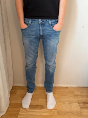 Replay Anbass jeans ljusblå, storlek 32 - Säljer ett par Replay Anbass jeans i ljusblå tvätt med snygga slitningar. Jeansen har rak passform och normal midja, med detaljerade sömmar på bakfickorna. Materialet är mjukt jeans-tyg som sitter skönt hela dagen. Är 183 cm på bilden. 