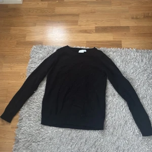 Svart stickad tröja  - Svart stickad tröja från Vila  med rund hals och långa ärmar. Enkel och stilren design som passar perfekt till jeans eller kjol. Tröjan har ribbade muddar vid ärmslut och nederkant för en snygg finish.