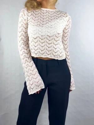 Vit spetscroppad topp – H&M XXS - Supersnygg vit spets/virkad topp från H&M i storlek XXS. Tröjan är uppklippt baktill för en unik och trendig look, samt har ett band på insidan som skyddar bysten, vilket gör att den sitter bättre och känns trygg att bära. Materialet är elastiskt och följsamt, vilket gör att den formar sig fint efter kroppen. Långa ärmar med lätt utsvängd passform ger en feminin och elegant vibe. Perfekt till fest, sommartillfällen eller stylad till vardags med kostymbyxor eller jeans. I mycket fint skick 🌸 