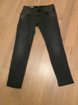 Mörkgråa Replay anbass jeans slim fit, stl 32/30 - Säljer ett par mörkgråa Replay anbass jeans i slim fit med klassisk femficksdesign. Jeansen har raka ben, snygga detaljer på bakfickorna och är tillverkade i ett mjukt jeansmaterial. Perfekta för dig som gillar en clean och stilren look. Endast använda en gång vilket betyder att de nästan är helt nya. Köpare står för frakt.