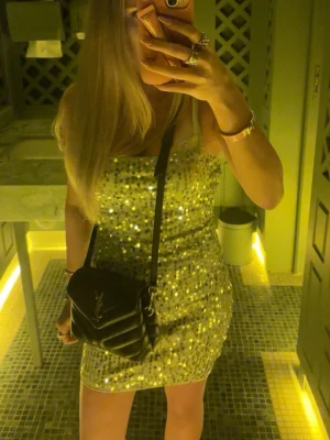 Glittrig kort klänning i silver - Supersnygg kort klänning med glittriga paljetter i silver. Klänningen är ärmlös med smala axelband och har en figurnära passform som verkligen sticker ut. Perfekt för dig som vill glänsa och synas. Materialet känns festligt och skimrande.