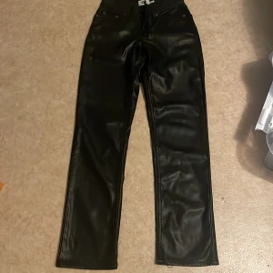Svarta raka byxor i skinnimitation - Säljer ett par svarta byxor från 157 i skinnimitation. Byxorna har raka ben, klassisk femficksmodell och normal passform. Snygg glansig finish och midjehällor för bälte. Perfekta för dig som vill ha en edgy look.