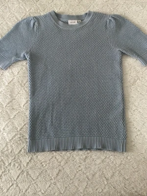 Ljusblå stickad topp - Säljer en söt ljusblå stickad tröja från VILA i storlek XS. Tröjan har korta ärmar, rund hals och ett snyggt strukturerat mönster. Aldrig använd 💖
