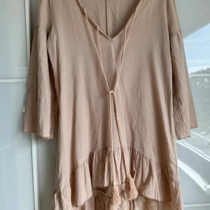 Beige Tunika från Oeuvre XS - Fin Tunika i XS, kanske i ”oversize”. Sömmen har gått upp på ett litet ställe annars i gott skick (se bild!). ca-mått i cm:	 axelbredd: 42 	 bröst: 46  längd:  korta sidan: 7 långa sidan: 86 framme: 67 bak: 82.