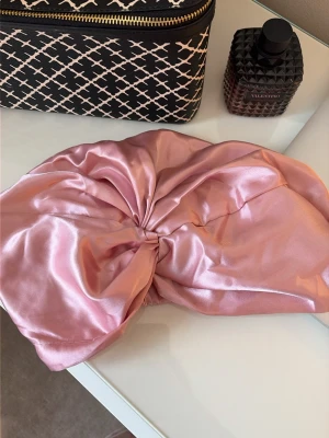 Rosa satin sovmössa - Snygg hårturban i glansigt rosa satinmaterial som är perfekt för att skydda håret under natten eller när du fixar din sminkrutin. Turbanen har en knut framtill och är mjuk och bekväm att bära. Passar alla hårtyper och ger en lyxig känsla.