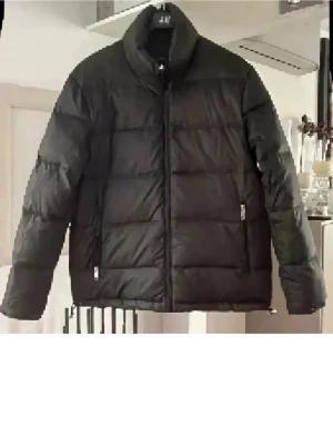 Dunjacka grön från Zara herr - Säljer en dunjacka  från Zara herr med hög krage och dragkedja framtill. Jackan har en boxig passform och breda, quiltade paneler som ger en riktigt fet look. Perfekt för kalla dagar när du vill vara både varm och stilren.