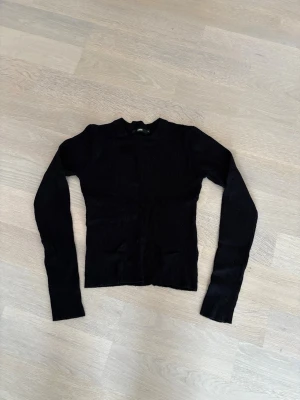 Svart ribbad långärmad tröja, BikBok - Säljer en svart ribbad tröja från BikBok med lång ärm och rund hals. Tröjan är i stretchigt material med smal passform och tillverkad av 80% viskos och 20% nylon. Perfekt till lager på lager eller som basplagg.