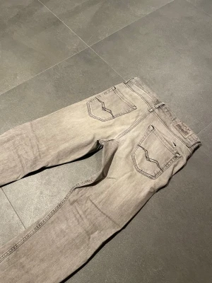 Replay grå jeans straight fit - Säljer ett par grå jeans från Replay med klassisk femficksdesign och snygga detaljer på bakfickorna. Jeansen har en rak passform och är tillverkade i mjukt jeanstyg. Perfekta för dig som gillar en clean och stilren look.
