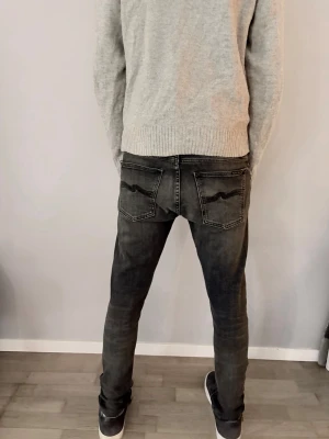 Svarta Nudie jeans tight Terry  w30/32l - Det här är ett par slim fit-jeans från NUDIE  med smala ben hela vägen från lår till fot. Passformen är tajt men ser ändå naturlig ut och följer benen utan att se överdrivet tight ut. Midjan sitter normalt och bakfickorna är placerade ganska högt, vilket ger en snygg och ren siluett bakifrån.  Färgen är en mörkgrå/svarttvättad denim med lätt slitning och mjuka tvättskiftningar, ett måste i varje garderob PRISET KAN DISKUTERAS 